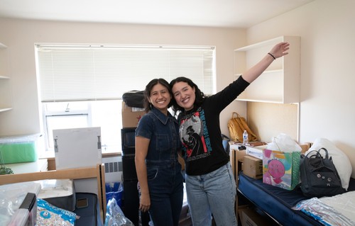 Two women standing in a dorm room.
