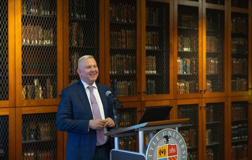 Provost Martin at a podium in front of a cabinet filled with books