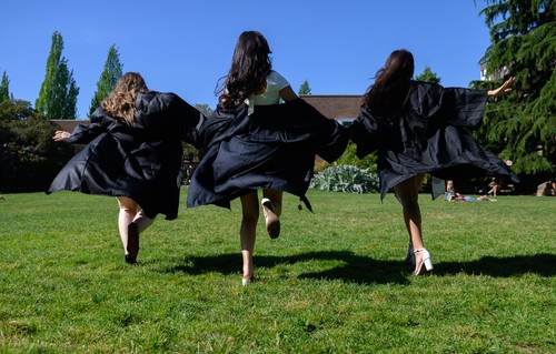 Three graduates in black gowns run across the grass, captured in motion from behind