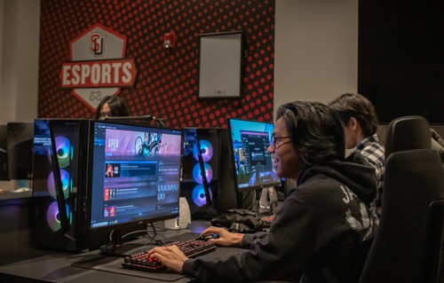 A group of people sitting at desks in a gaming room.