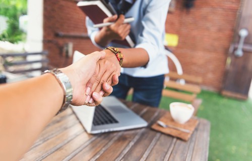 Two executives shaking hands over a laptop