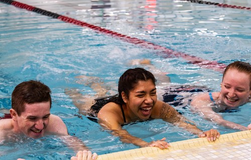 3 students hanging onto the pool wall kicking