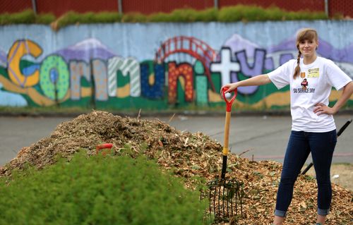 Faculty holding shovel by leaf pile smiling in front of painted mural that says 