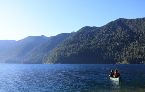 Two students with lifejackets row in a canoe on Lake Crescent with trees in the background