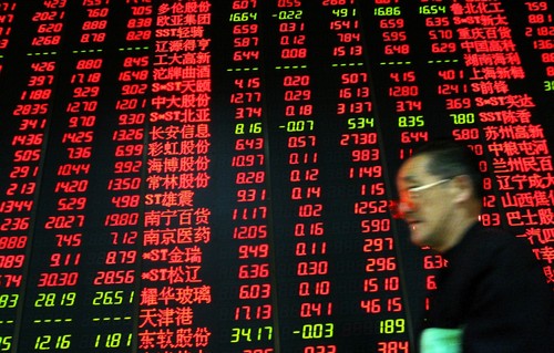 An elderly man walks past a screen showing share prices at stock brokerage in Lanzhou, China