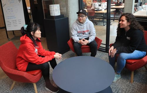 Three students sit and talk around table