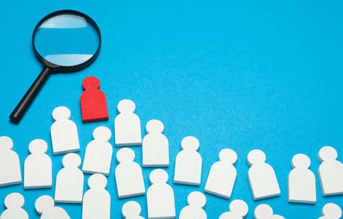 Many small white figures and one red figure with a magnifying glass, signifying standing out from the crowd