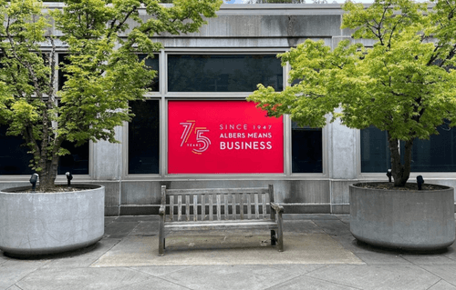 Pigott Building with trees and a bench, a sign in the window reads: 75 years, since 1947 Albers means Business