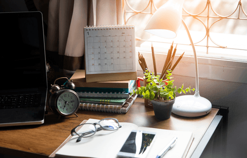 A desk with lamp, notebooks, calendar, clock, and laptop