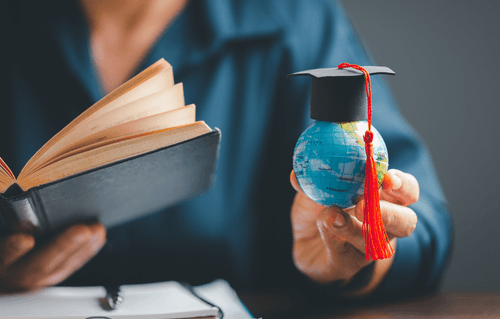 Student holding a book and a small globe wearing a mortarboard