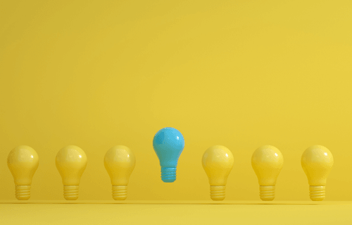 A blue lightbulb stands out at the center of a row of yellow lightbulbs on a yellow background, symbolizing leadership and standing apart.