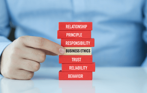 A hand holding a block that says Business Ethics, surrounded by blocks that say Relationship, Principle, Responsibility, Trust, Reliability, and Behavior