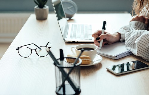 Woman studying at desk with glasses, laptop, and coffee