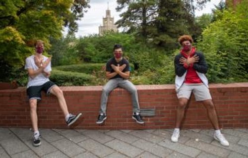 A photo of three male basketball athletes on campus wearing masks and forming their hands into the Redhakw symbol