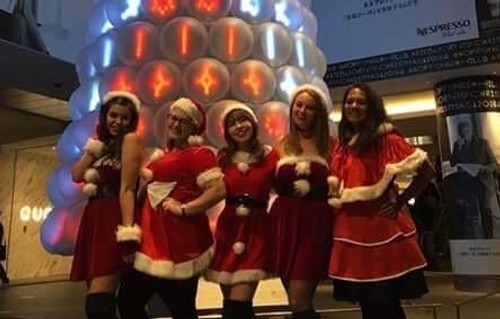 Nina and three friends stand in front of a Christmas tree in Santa outfits.
