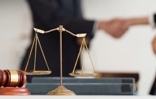 A gavel next to scales with two people shaking hands in the background