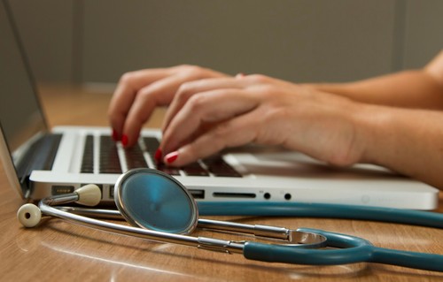 Hands typing on a laptop with stethoscope in foreground
