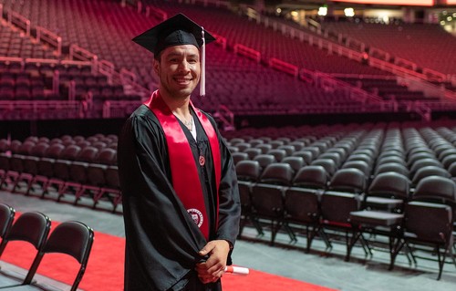 Student standing in cap and gown at commencement smiling at camera