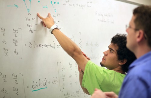 A group of students in a classroom writing on a whiteboard.