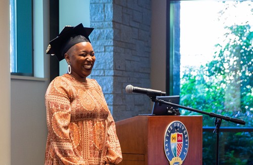 A woman in front of a podium at graduation ceremony wearing commencement regalia cap