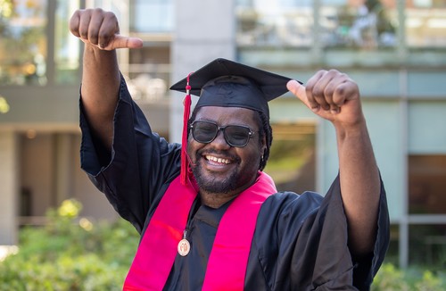 SU grad in regalia giving a smile and two thumbs up